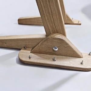 May include: Close-up of the wooden base of a chair or table. The base is made of light brown wood and has a triangular shape. There are several screws visible on the base.