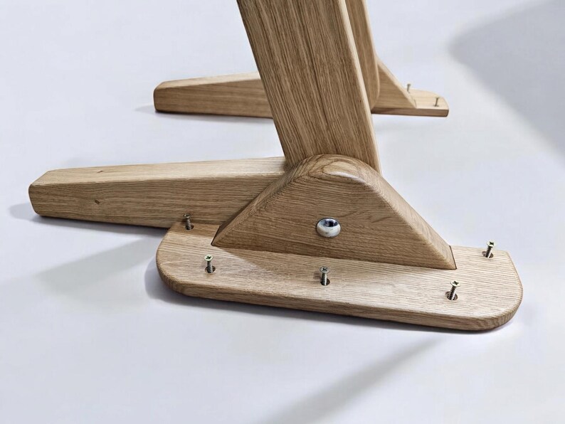 May include: Close-up of the wooden base of a chair or table. The base is made of light brown wood and has a triangular shape. There are several screws visible on the base.