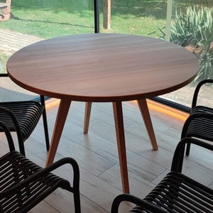May include: A round wooden table with four black chairs. The table has a natural wood finish and the chairs have a woven design.