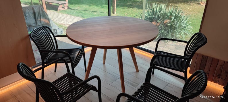 May include: A round wooden table with four black chairs. The table has a natural wood finish and the chairs have a woven design.