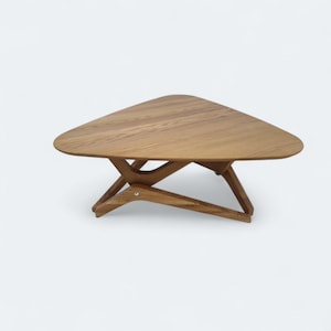 Könnte beinhalten: Ein Couchtisch aus Holz mit dreieckiger Tischplatte und einem einzigartigen, abgewinkelten Beingestaltung. Der Tisch ist aus hellem Holz gefertigt, das die natürliche Maserung zeigt. Die Abmessungen des Tisches betragen ca. 76 cm Breite und 38 cm Höhe.