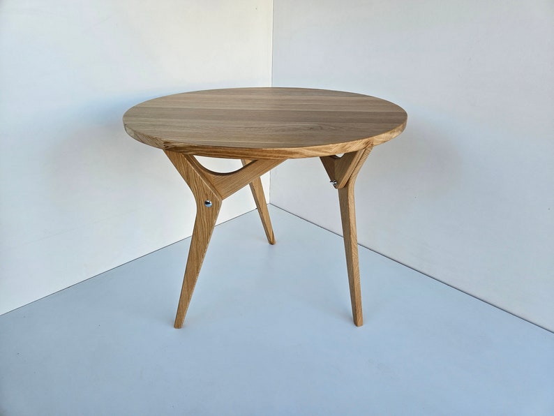 May include: A round wooden table with a light brown finish and a unique, angled, tripod base.