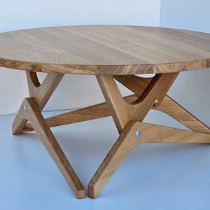 May include: A round wooden coffee table with a natural wood finish. The table has a unique X-shaped base made of solid wood.