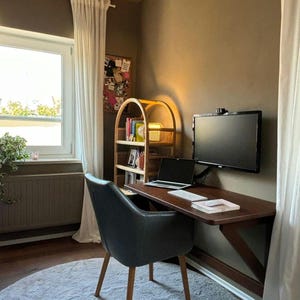 May include: A home office workspace with a dark wood folding desk mounted to the wall. A black office chair sits in front of the desk. A laptop computer and a black monitor are on the desk. A white rug is on the floor. A small bookshelf with a woven basket is in the corner.