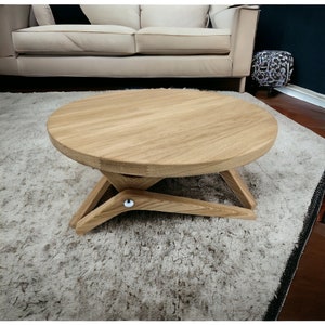 May include: A round wooden coffee table with a unique X-shaped base. The table is made of light brown wood and has a smooth, polished finish.