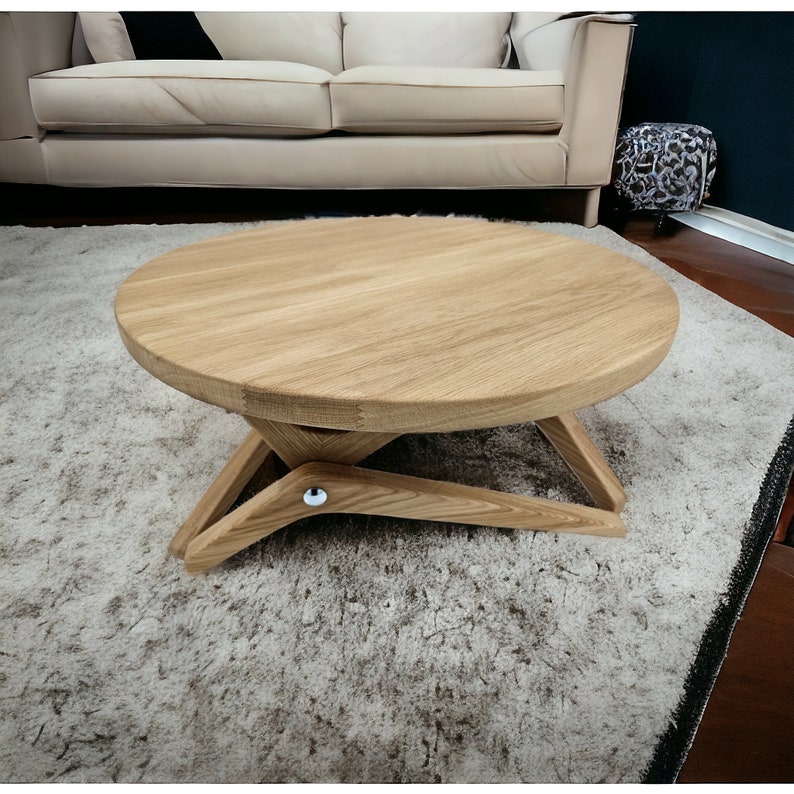 May include: A round wooden coffee table with a unique X-shaped base. The table is made of light brown wood and has a smooth, polished finish.