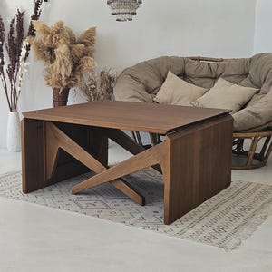 Peut inclure: Une table basse en bois foncé avec un design en X unique. La table a un plateau rectangulaire et est faite de bois massif.