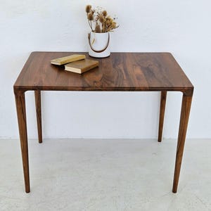 May include: A rectangular wooden table with four legs. The table top is made of dark wood with a natural grain pattern. Two books are placed on the table top.