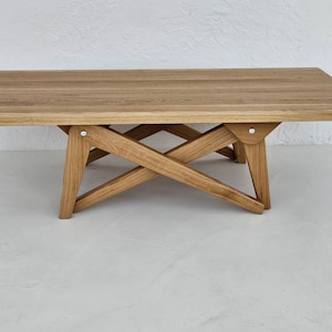 May include: A wooden coffee table with a rectangular top and a unique X-shaped base. The table is made of light brown wood and has a natural finish.