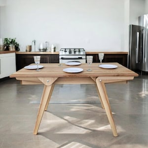 May include: A light wood dining table with a natural finish. The table has a rectangular top and four legs. There are four white plates and four glasses on the table.