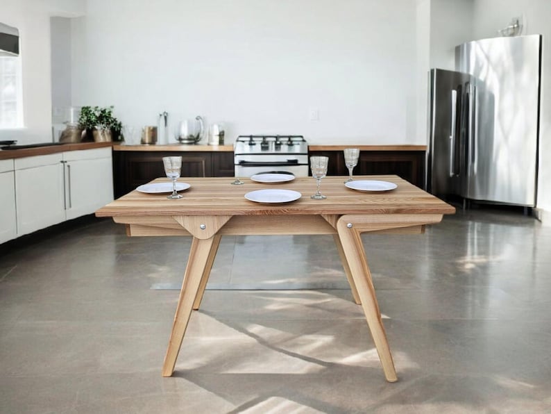 May include: A light wood dining table with a natural finish. The table has a rectangular top and four legs. There are four white plates and four glasses on the table.
