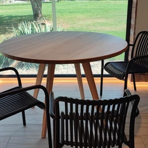 May include: A round wooden table with four black chairs. The table and chairs are in a room with a large window overlooking a grassy area.