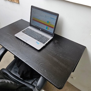 May include: A black wooden desk with a laptop computer on top. The desk is mounted to a wall and has a wood grain pattern. The laptop is open and has a blank screen.