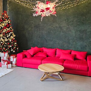 May include: A red sofa with a wooden coffee table in front of a green wall decorated with a white and pink floral chandelier and a Christmas tree with red and white ornaments.