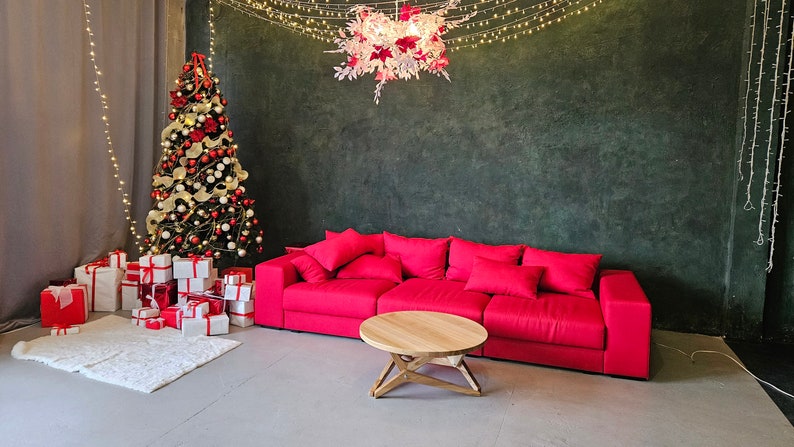May include: A red sofa with a wooden coffee table in front of a green wall decorated with a white and pink floral chandelier and a Christmas tree with red and white ornaments.