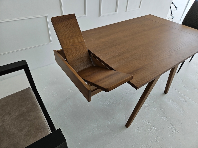 Puede incluir: Una mesa de madera marr&oacute;n con una hoja que se pliega hacia abajo para crear asientos adicionales. La mesa tiene un dise&ntilde;o simple con cuatro patas y una tapa rectangular.