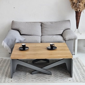 Könnte beinhalten: Ein grauer Couchtisch mit einer Holzplatte und einem Kreuzfuß. Zwei Kaffeetassen mit Untertassen stehen auf dem Tisch.