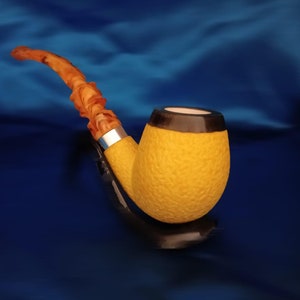 Puede incluir: Una pipa de tabaco amarilla con una cazoleta marrón y negra y una boquilla marrón. La pipa está sobre una superficie azul.