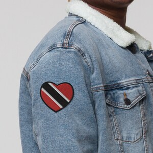 May include: A light blue denim jacket with a white sherpa collar and a red heart-shaped patch with the flag of Trinidad and Tobago on the left sleeve.