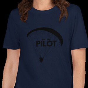 May include: A navy blue t-shirt with a black graphic of a paraglider and the text "Just the Pilot".
