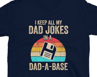 May include: A navy blue t-shirt with a retro-style graphic of a floppy disk and the text "I keep all my dad jokes in a dad-a-base".