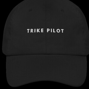 May include: A black baseball cap with white embroidered text that reads "TRIKE PILOT".