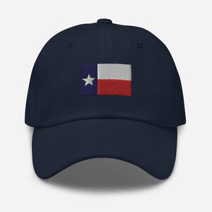 May include: A navy blue baseball cap with an embroidered Texas flag on the front. The flag is red, white, and blue with a single white star in the blue section.
