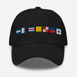 Puede incluir: Gorra de béisbol negra con banderas de señales náuticas bordadas en azul, blanco, rojo y amarillo. La gorra tiene una visera curva y una corona estructurada. Un accesorio elegante para los entusiastas del mar.