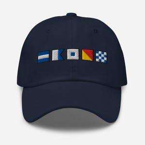 Puede incluir: Gorra de béisbol azul marino con banderas de señales náuticas bordadas en blanco, azul y amarillo. La gorra tiene una visera curva y una correa ajustable. Un accesorio elegante.