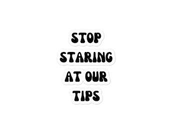 May include: A sticker with the text "STOP STARING AT OUR TIPS" in black letters on a white background.