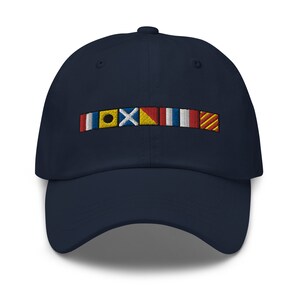 Puede incluir: Una gorra de béisbol azul marino con una fila de banderas de señales náuticas de colores bordadas en la parte delantera.