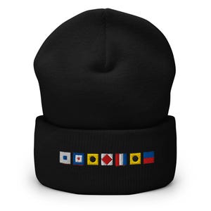 Puede incluir: Gorro negro con banderas de señales náuticas bordadas en el borde. Las banderas son de varios colores, incluyendo blanco, azul, rojo y amarillo. El gorro está hecho de un material suave y tejido.