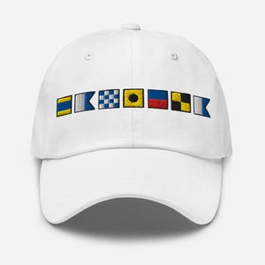 Può includere: Cappellino da baseball bianco con bandiere nautiche ricamate in giallo, blu, rosso e nero. Le bandiere sono disposte orizzontalmente sulla parte anteriore, aggiungendo un tema marittimo. Il cappellino ha una visiera curva e uno stile casual.