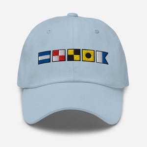 Puede incluir: Gorra de béisbol azul claro con banderas de señales náuticas bordadas. Las banderas son de varios colores, incluyendo azul, rojo, negro, amarillo y blanco. La gorra tiene una visera curva y un cierre de correa de tela.
