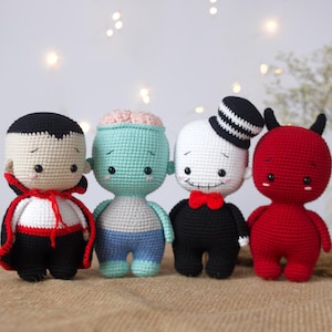 May include: Four crocheted Halloween character toys. A vampire, a Frankenstein, a skeleton, and a devil. Each toy has a cute, cartoon-like face and is dressed in a costume.