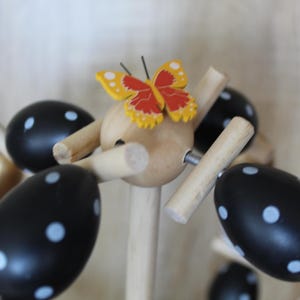 May include: Wooden Easter egg tree featuring black eggs with white polka dots, and a gold egg with white polka dots. A yellow and red butterfly decorates the top. The tree is made of wood with a light brown background.