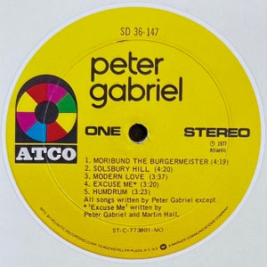 May include: A yellow vinyl record with a rainbow circle in the center. The record is labeled "Peter Gabriel" and "One" with the song titles "Moribound the Burgermeister", "Solsbury Hill", "Modern Love", "Excuse Me", and "Humdrum". The record is from 1977 and is on the ATCO label.