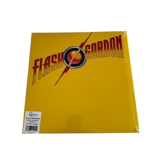 May include: A yellow vinyl record album titled "Flash Gordon" by Queen. The album cover features the title in a bold, red and gold font with a lightning bolt and a planet graphic. The album is sealed in plastic.