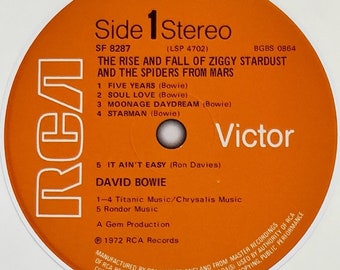 May include: Orange vinyl record label with the text "Side 1 Stereo" and "The Rise and Fall of Ziggy Stardust and the Spiders from Mars" by David Bowie. The record label also includes the track listing and credits.