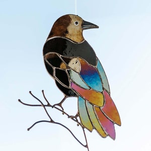 May include: A stained glass bird with iridescent wings, perched on a branch, hangs from a clear suction cup against a blue sky.