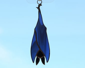 May include: A blue stained glass bat hanging from a clear suction cup hook against a light blue background.