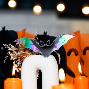 May include: A black iridescent stained glass bat with a white, speckled ceramic vase and lit candles in the background.