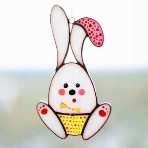 May include: A white stained glass bunny with red polka dot ears and a yellow polka dot diaper. The bunny has black eyes and a red nose.
