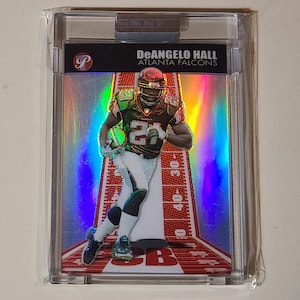 May include: A DeAngelo Hall Atlanta Falcons football card in a protective case. The card features a player in a Falcons uniform, holding a football. The background has a football field design with yard markers.