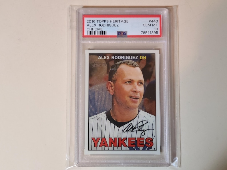 May include: A baseball card featuring Alex Rodriguez in a New York Yankees uniform. The card is encased in a protective holder and includes the text "2016 Topps Heritage" and "Yankees". The card is graded as GEM MT 10.