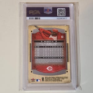 May include: A baseball card encased in a clear plastic holder. The card features a player in a red uniform, with the number 13. The card is labeled "Ken Griffey Jr." and includes statistics. The holder has a PSA label.