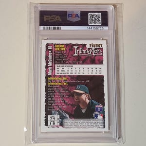 May include: A PSA-graded Mark McGwire baseball card encased in a clear plastic holder. The back of the card features a purple background, a photograph of the player in an Oakland Athletics cap, and printed statistics and biographical information.