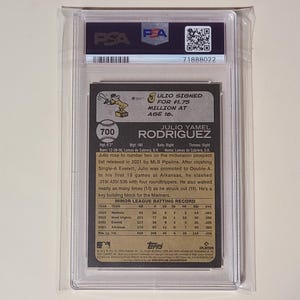 May include: A baseball card encased in a protective holder. The card features text about Julio Rodriguez, including his name, statistics, and a Topps logo. The card is graded and authenticated by PSA.