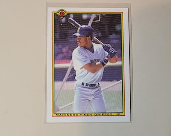 May include: Baseball card depicting Ken Griffey Jr. of the Seattle Mariners, in a batting stance. The card has a green and yellow border, with the Bowman logo. Text at the bottom reads "MARINERS KEN GRIFFEY, JR."
