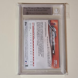 May include: A baseball card of Shohei Ohtani in a protective case. The card features the Topps logo and the Angels team logo. The case has a Beckett Grading Services label.